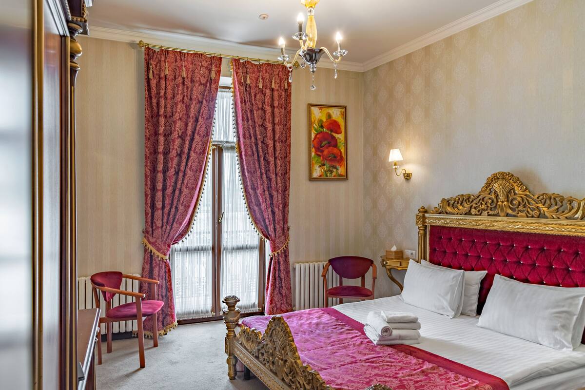 Un dormitorio con una cama grande, un cabecero decorado y cortinas rojas.