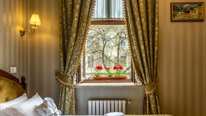 A hotel room with a bed, a window with curtains, a radiator, and a wall-mounted light fixture. - Saint Feder (Lviv)