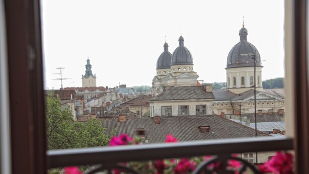 A view of a cityscape with prominent domed buildings and a balcony with flowers. - Saint Feder (Lviv)