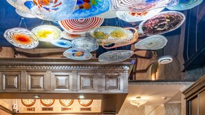 En luksuriøs hotellobby med et stort mosaikmaleri, en imponerende lysekrone og et klassisk ur.