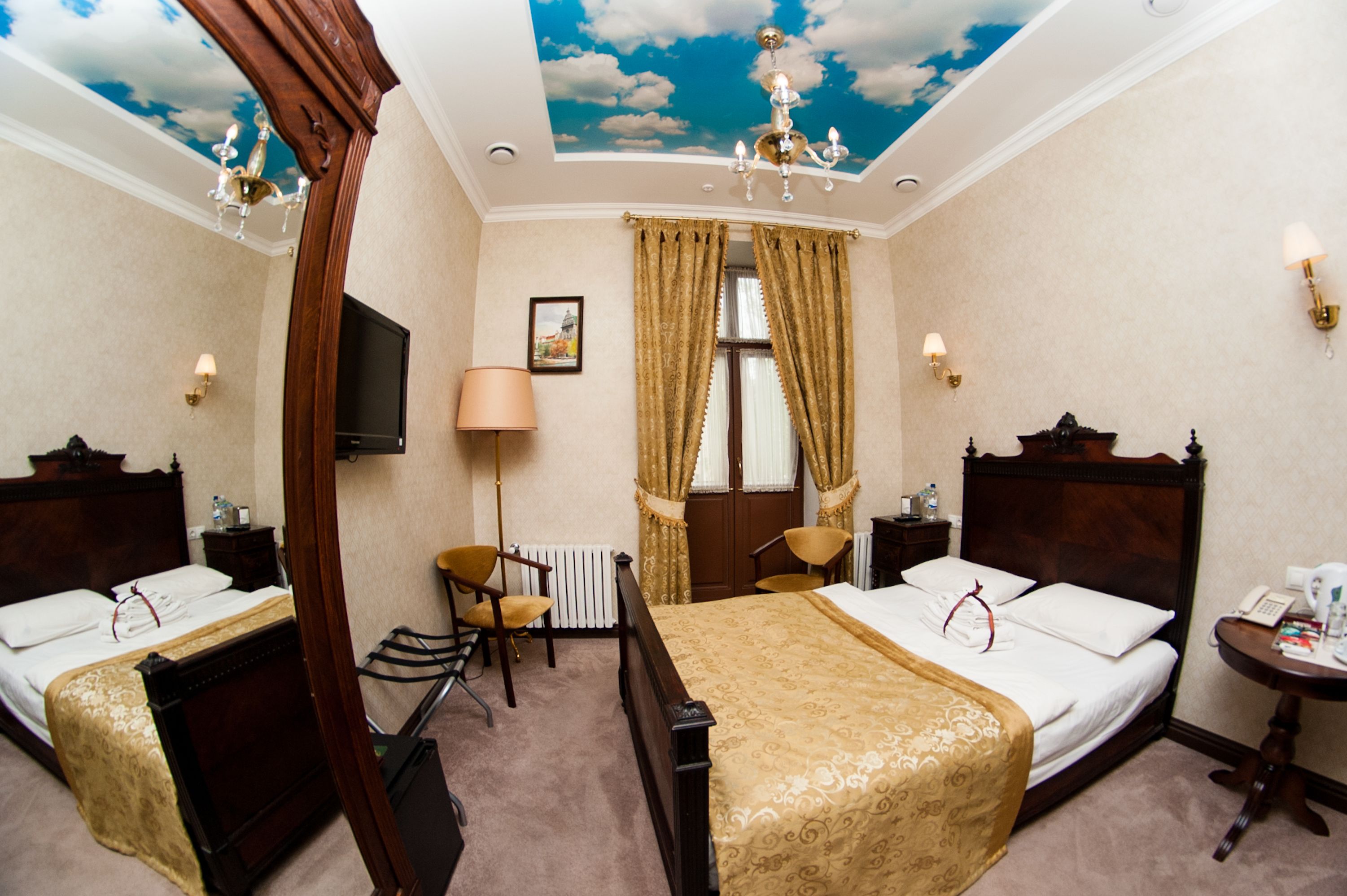 Ein Hotelzimmer mit zwei Betten, einer Deckenmalerei, einer Chandelüster und einem kleinen Tisch mit einer Lampe.