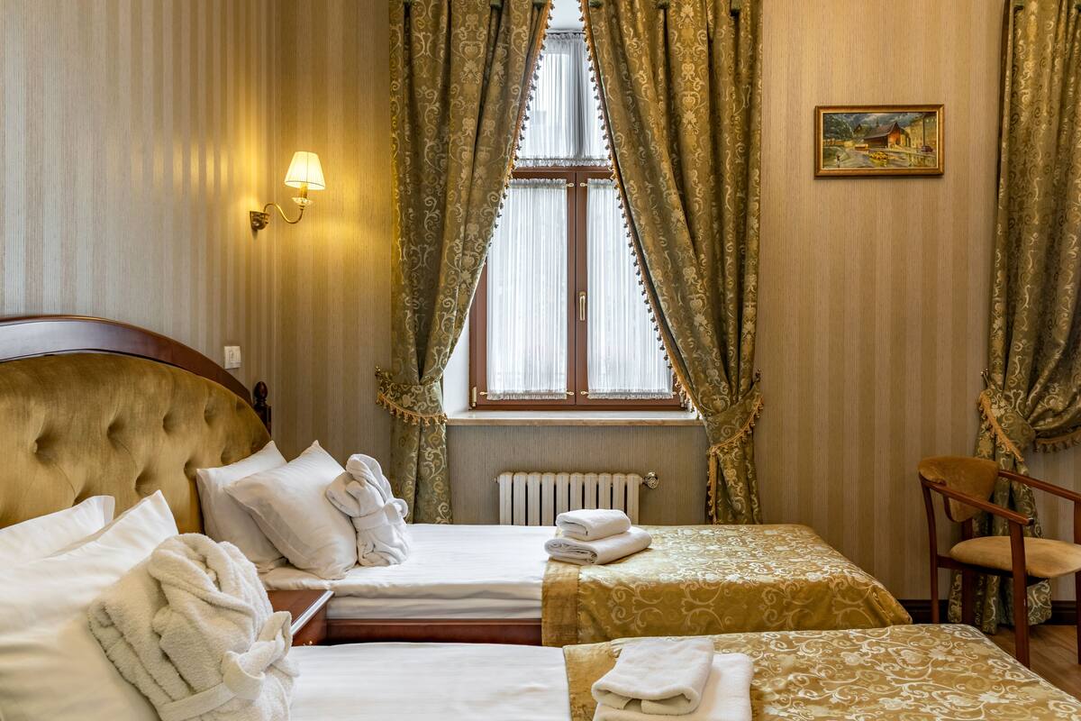 Habitación de hotel con dos camas, un radiador, una lámpara de pared y una silla.