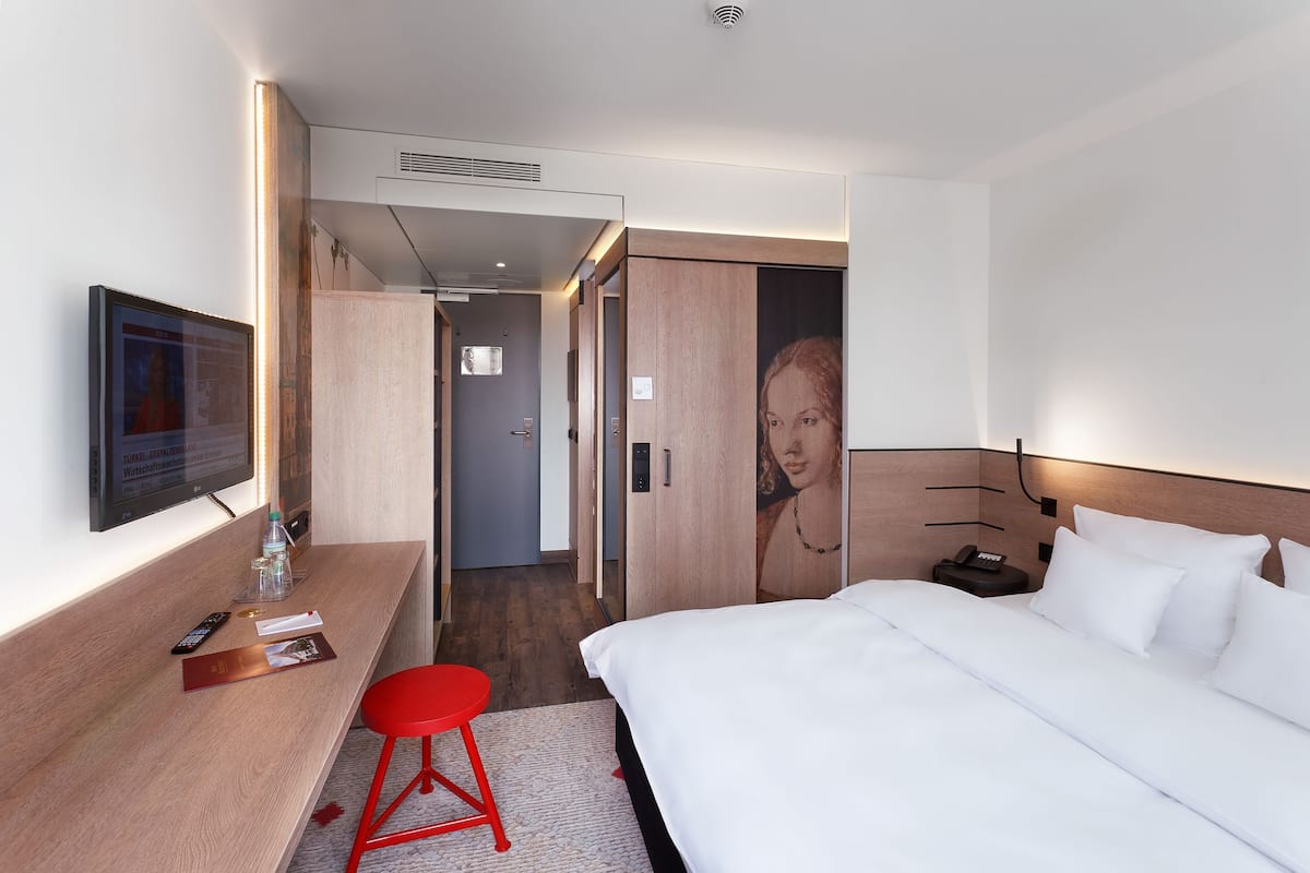 Ein modernes Hotelzimmer mit Bett, Fernseher, Schreibtisch und einem roten Sessel.