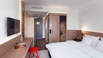 Una habitación de hotel moderna con una cama, un televisor, un escritorio y una silla roja.