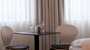 A hotel room with a bed, two chairs, a small table with a bottle and glasses, and sheer curtains.