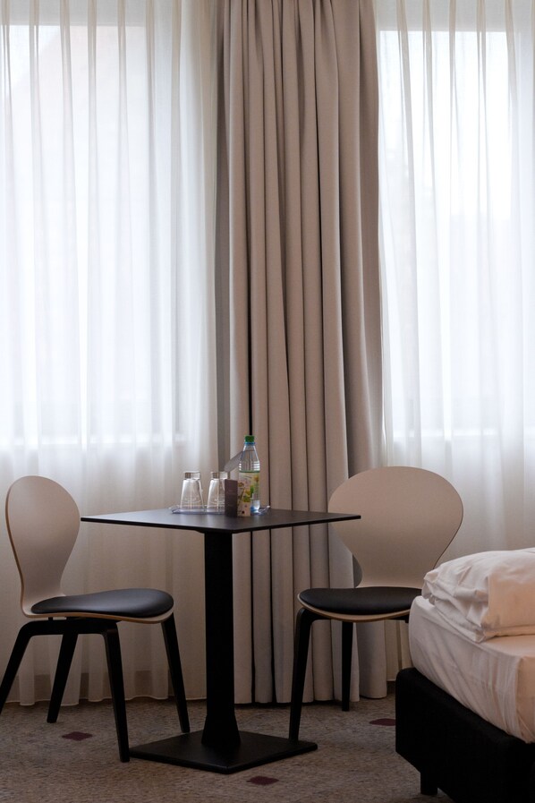 A hotel room with a bed, two chairs, a small table with a bottle and glasses, and sheer curtains. - Sorat Hotel Saxx Nürnberg (Nuremberg)