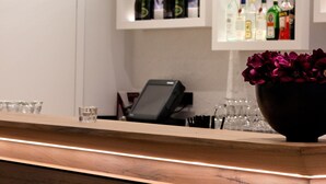 A bar area with a wooden counter, bar stools, a glass display case with bottles, and a bowl of flowers.