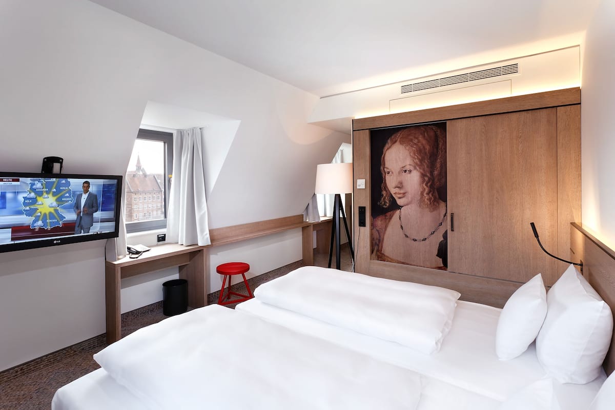 Ein Hotelzimmer mit Bett, Schreibtisch, Fernseher und Fenster.