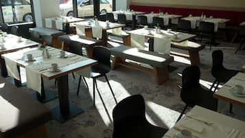 A restaurant with multiple tables and chairs, arranged in a spacious layout with large windows providing a view of the street outside.