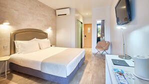 A modern hotel room with a large bed, a flat-screen TV mounted on the wall, a desk with a lamp, and a chair.