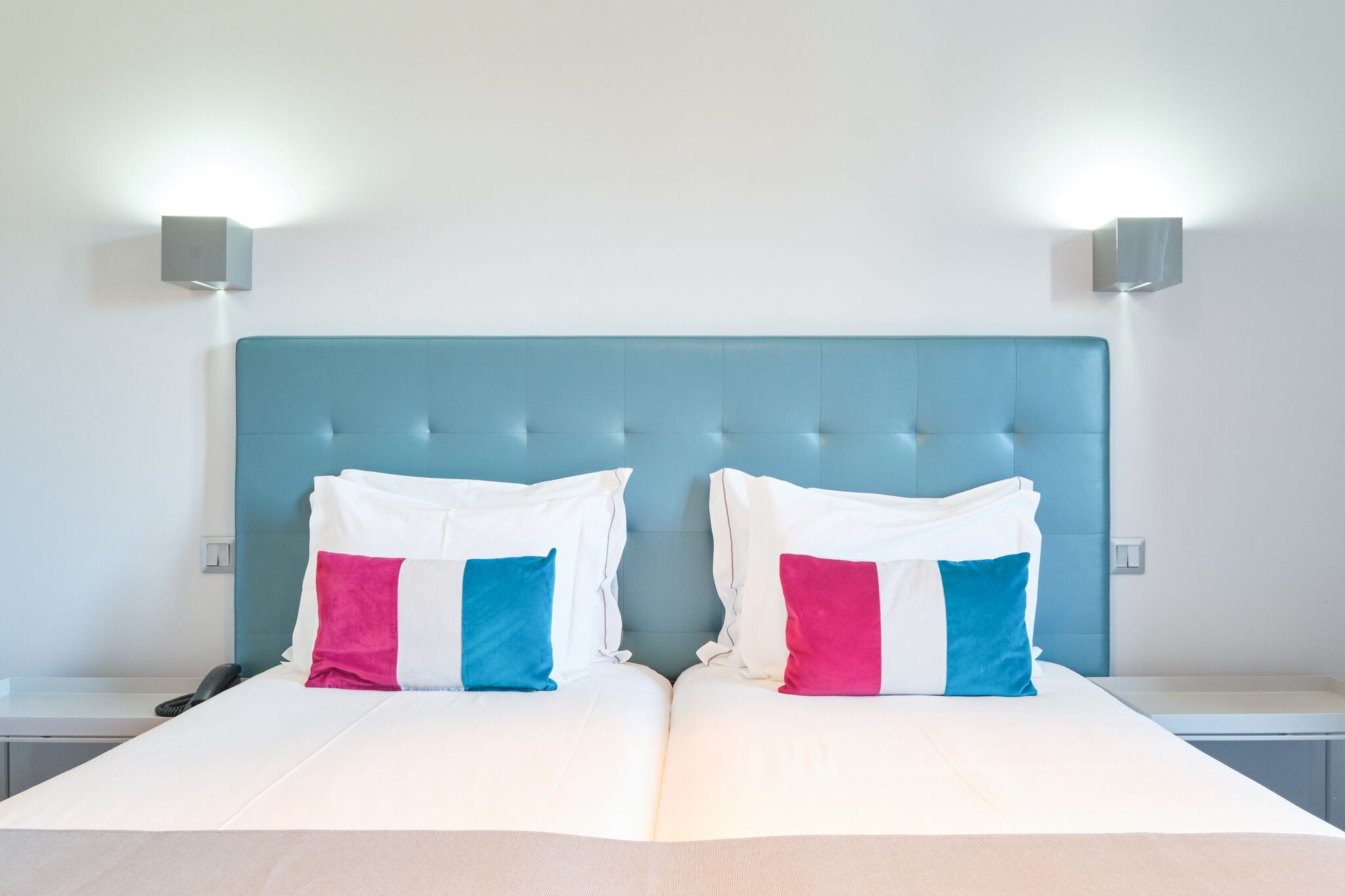 A neatly made double bed with a tufted headboard, two bedside tables, and two wall-mounted light fixtures.
