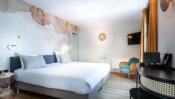Una habitación de hotel moderna con una cama grande, una mesa de comedor redonda, un televisor y una lámpara fijada a la pared.