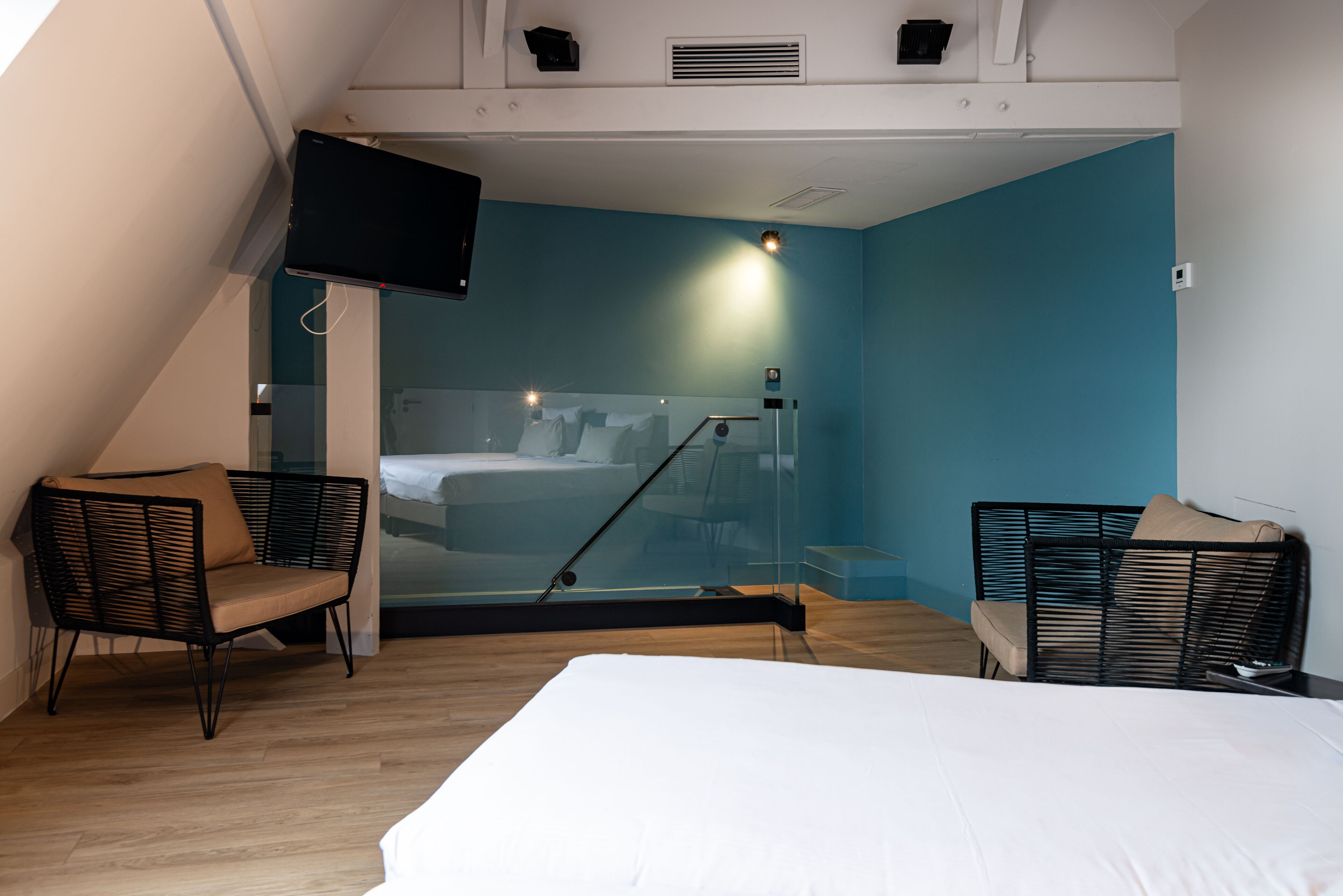 Moderni hotellihuone, jossa on sänky, kaksi tuolia, televisio ja suuri ikkuna.