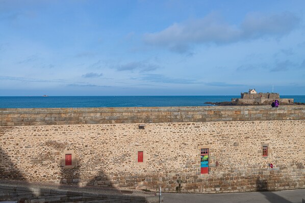 A stone wall with red doors and windows, overlooking a body of water. - Hôtel de la Cité (Saint-Malo)