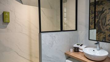 A modern bathroom with a marble floor, a wooden vanity, a white sink, and a large mirror.