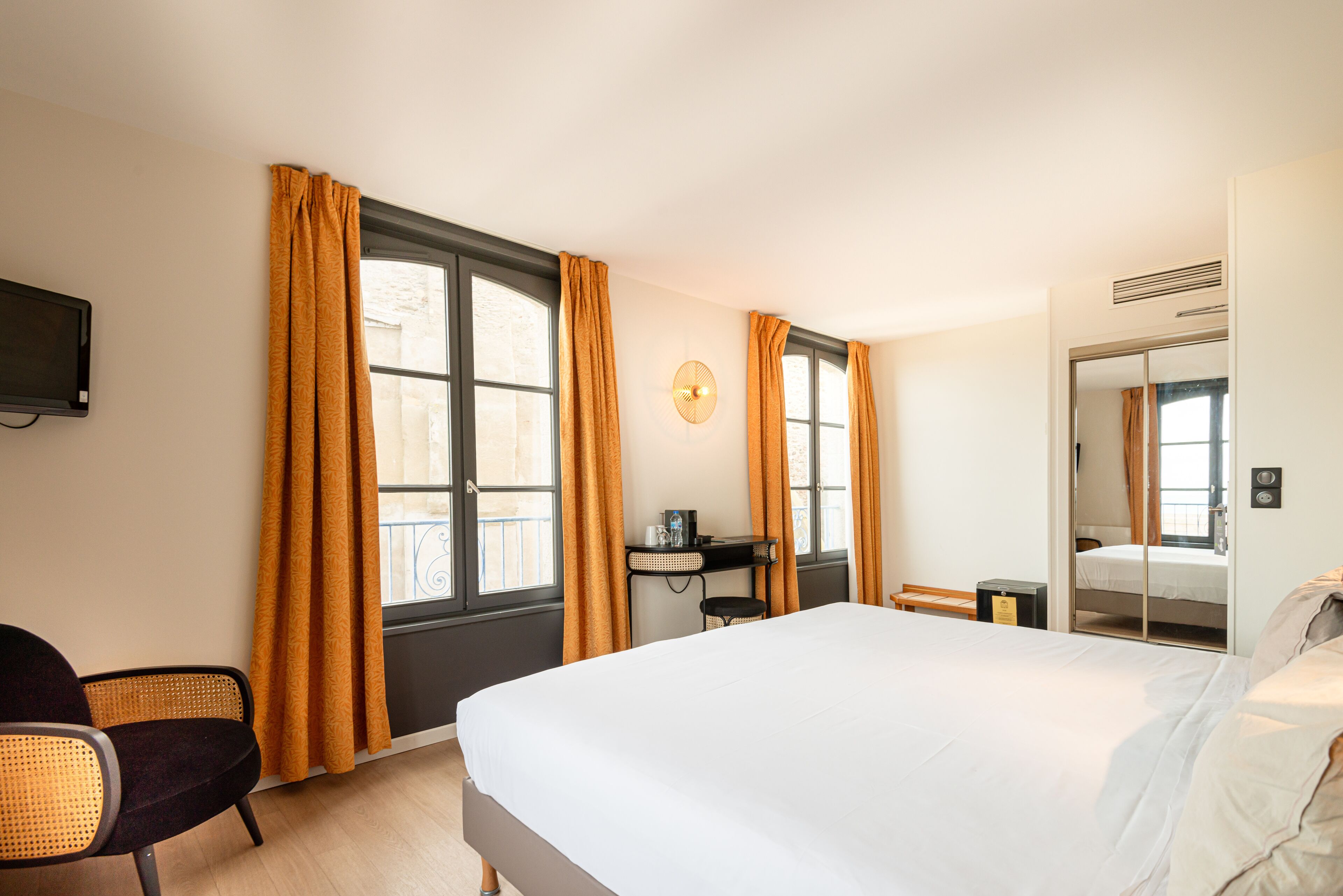 Habitación de hotel con una cama grande, un escritorio con silla, un televisor montado en la pared y un armario.