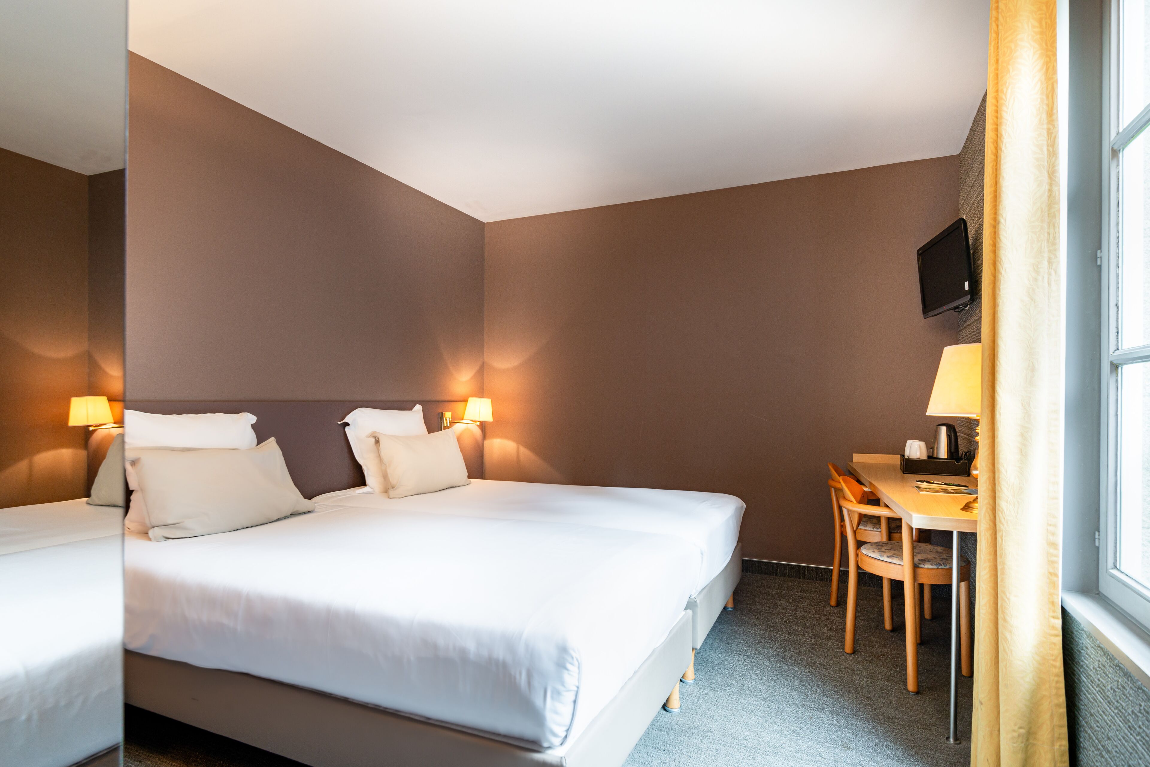 A hotel room with two beds, a desk with a chair, a television, and a window with curtains.
