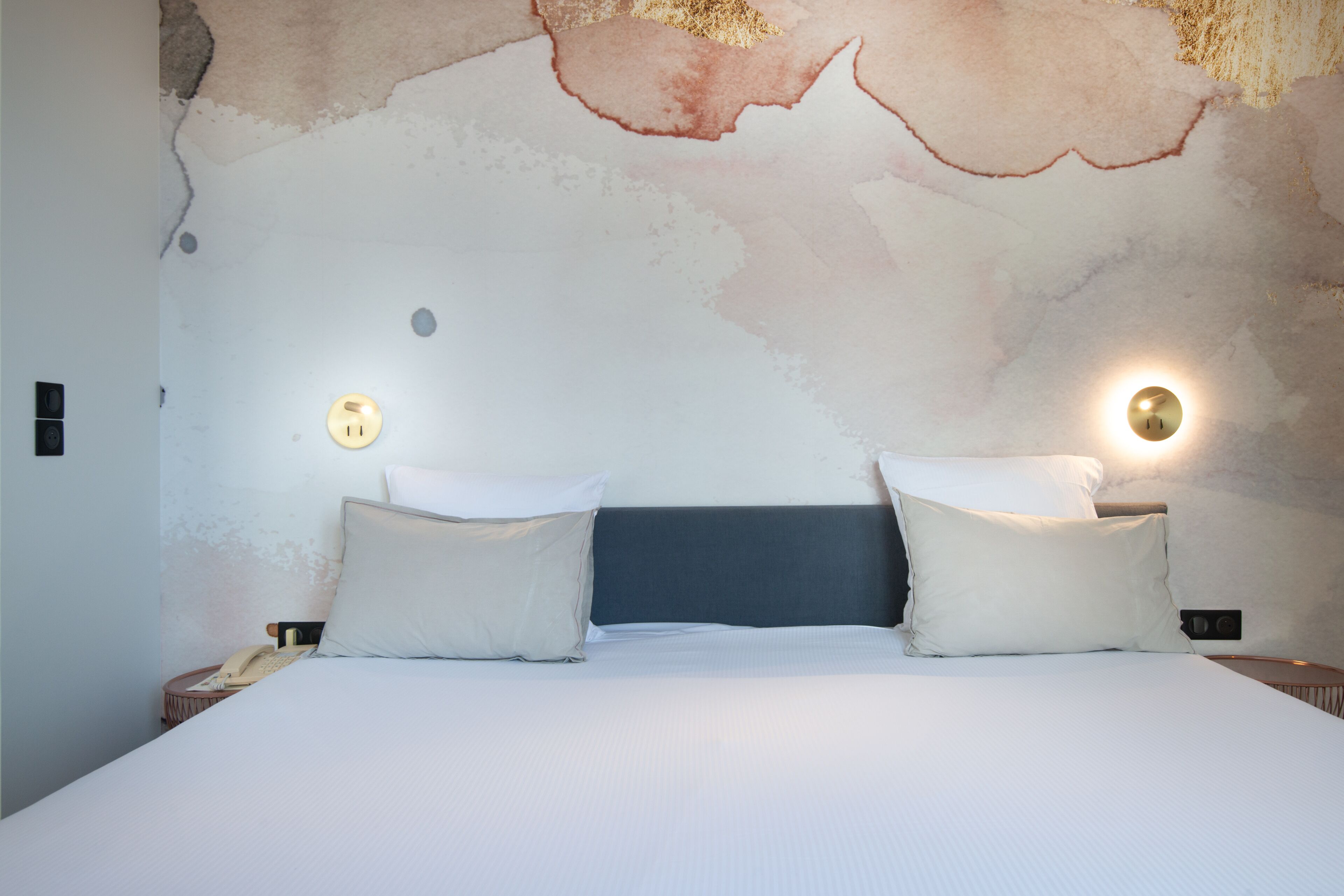 Un lit avec deux oreillers, une tête de lit et un mur orné d’un motif texturé.