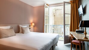 Habitación de hotel con cama, escritorio, silla, televisor y balcón con vistas.