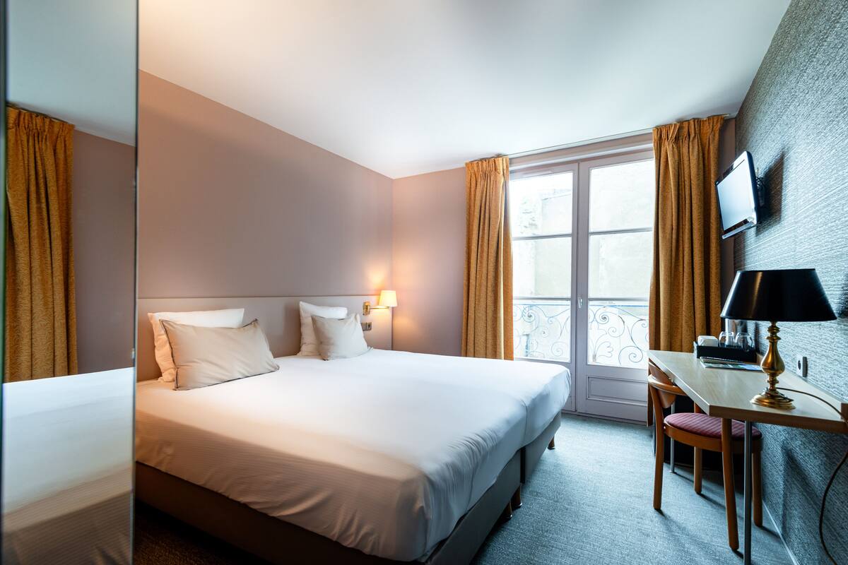 A hotel room with a large bed, a desk with a lamp, and a TV on the wall.