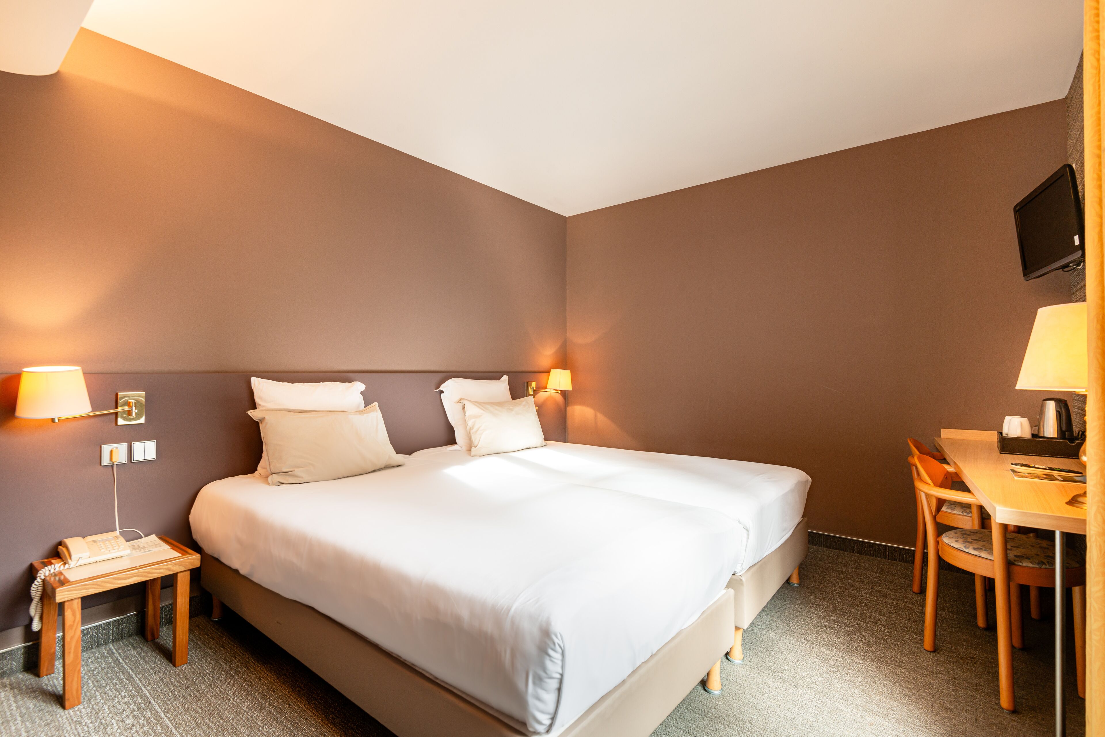 Quarto de hotel com cama grande, mesas de cabeceira, escrivaninha e televisão.