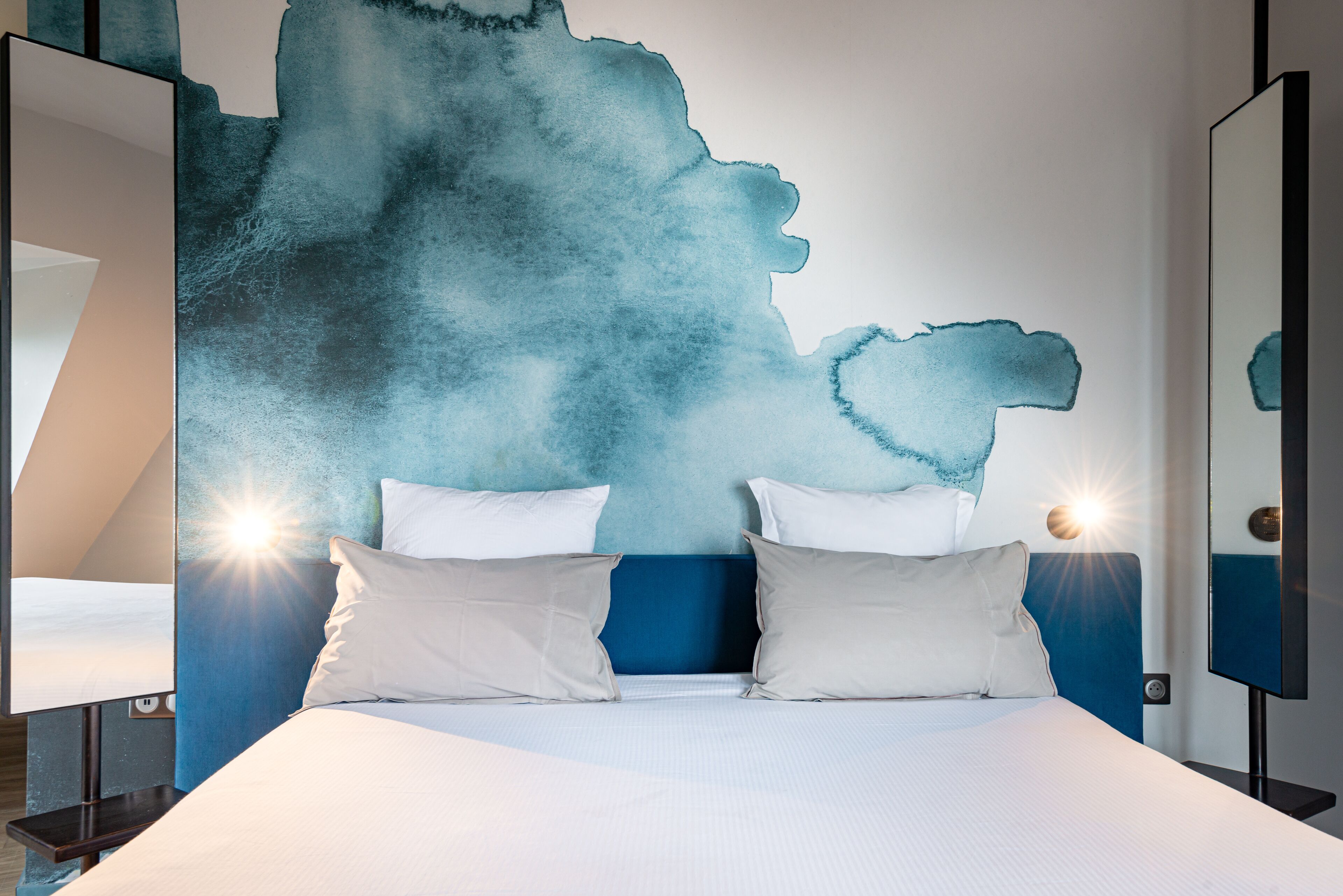 Une chambre moderne avec un grand lit, deux tables de chevet et une fresque murale.