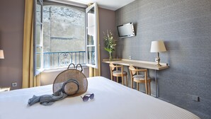 Una habitación de hotel con cama, escritorio, silla, televisor y ventana con cortinas.