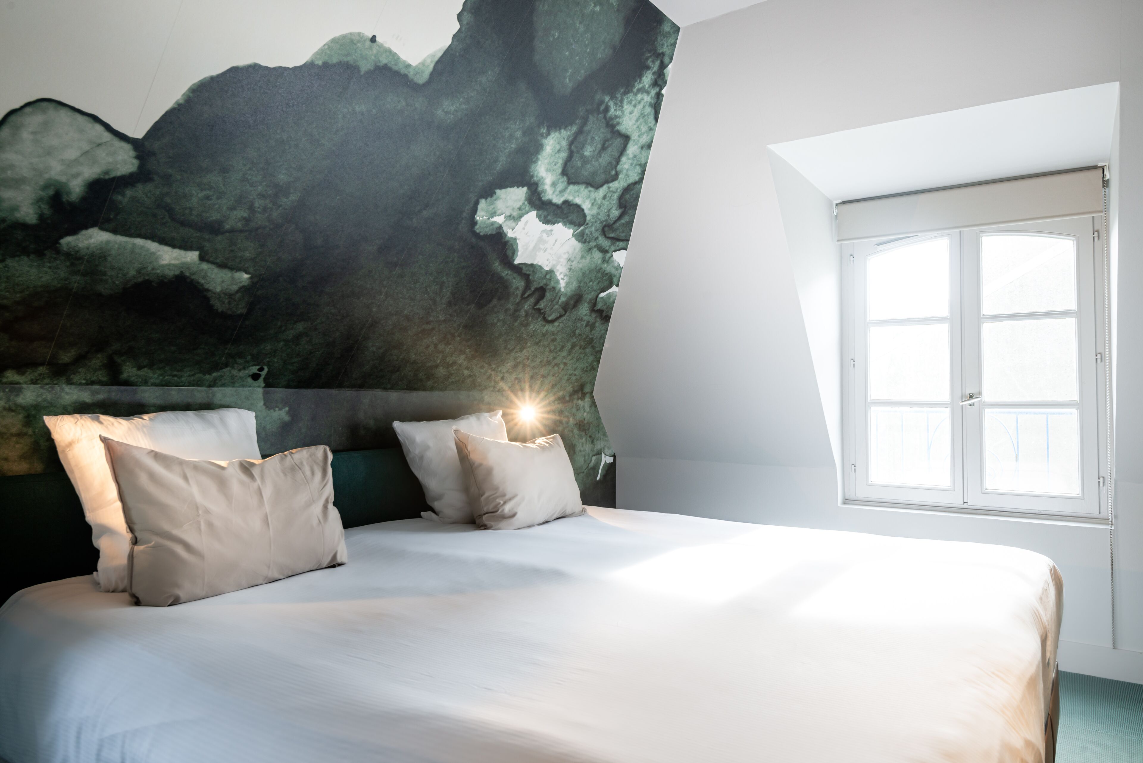 Un dormitorio con una cama grande, dos almohadas, un cabecero con un mural texturizado en la pared y una ventana con contraventanas blancas.