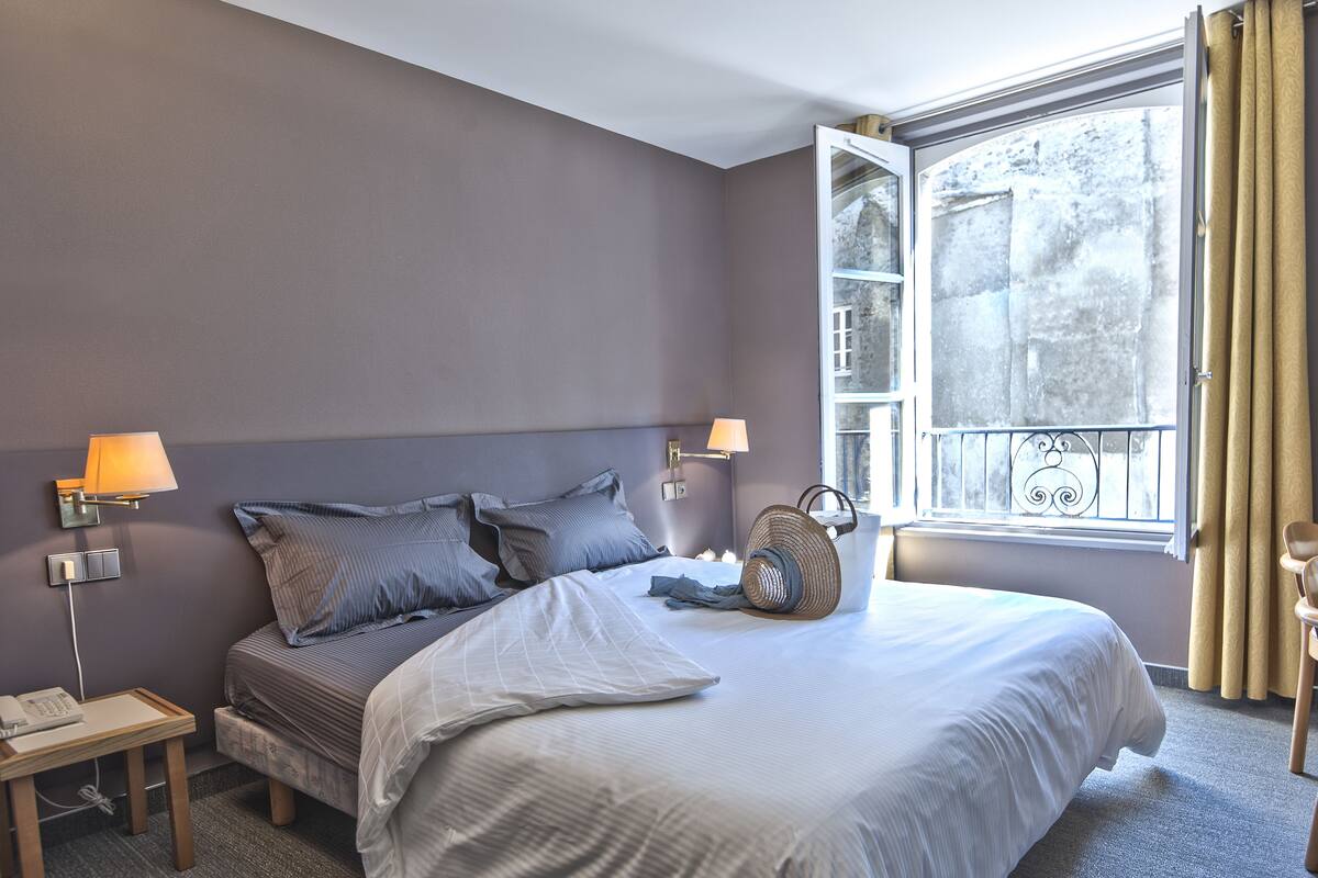 A bedroom with a large bed, two bedside lamps, a bedside phone, and a window with curtains.