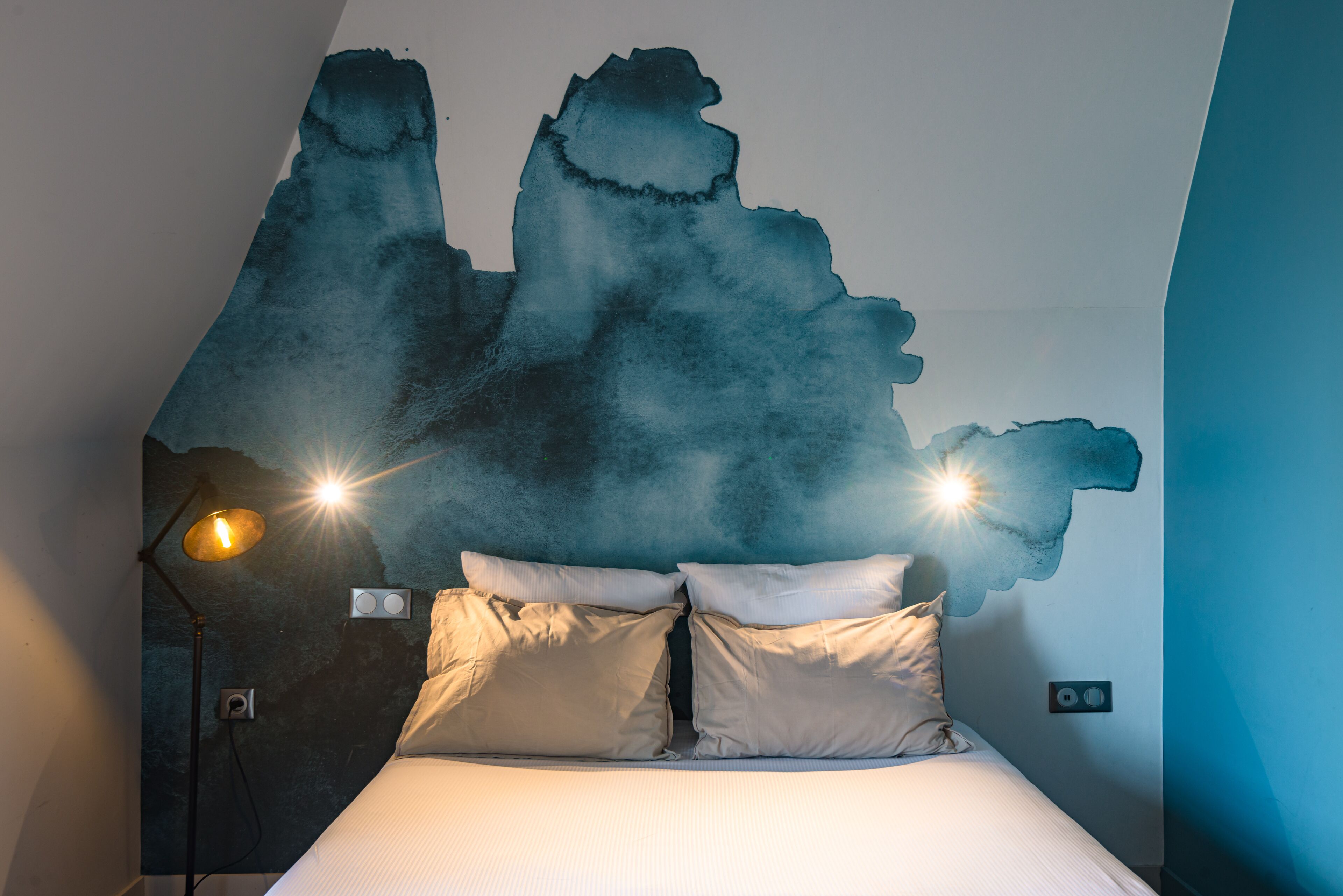 Quarto com cama, duas luminárias de cabeceira e um aplique na parede.