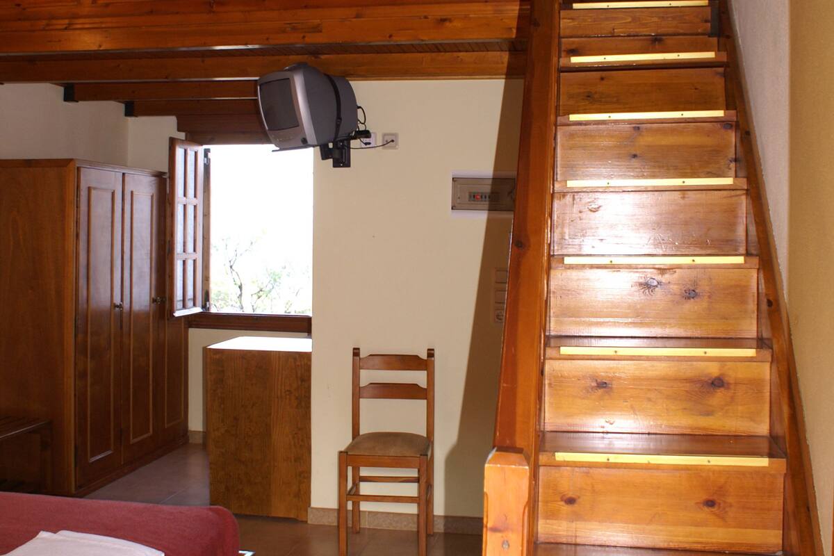 Un dormitorio con una cama y una silla de madera, una escalera de madera y un televisor montado en la pared.