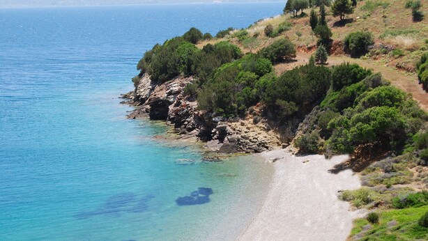 A coastal landscape with a clear beach, rocky cliffs, and dense greenery. - Drymna Hotel (Dorida)