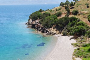 A coastal landscape with a clear beach, rocky cliffs, and dense greenery. - Drymna Hotel (Dorida)