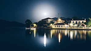 A waterfront property with a boat dock, buildings with multiple stories, and a calm lake reflecting the moonlight. - Drymna Hotel (Dorida)
