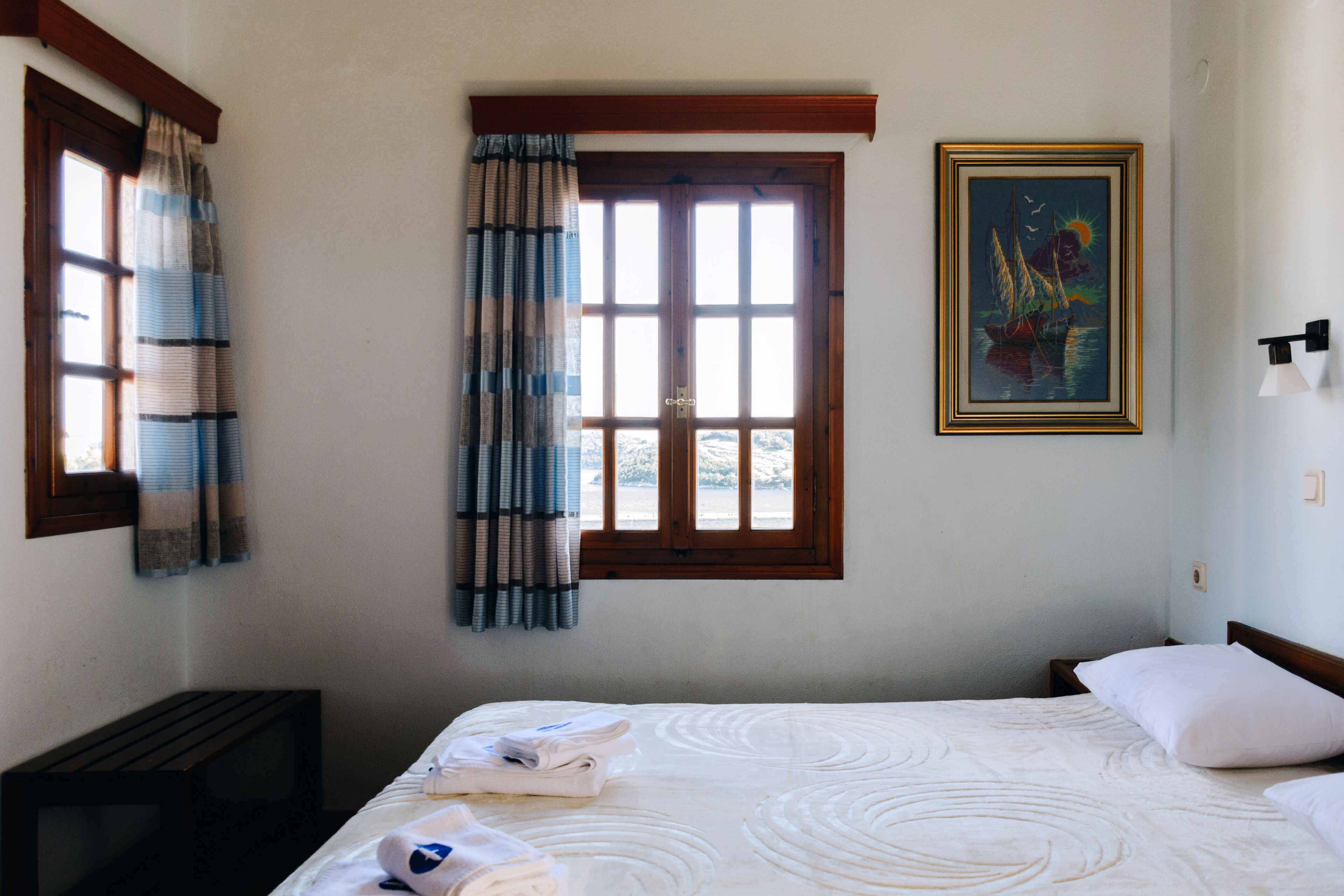 Habitación de hotel con cama, ventana con cortinas, un cuadro en la pared y una mesita de noche.