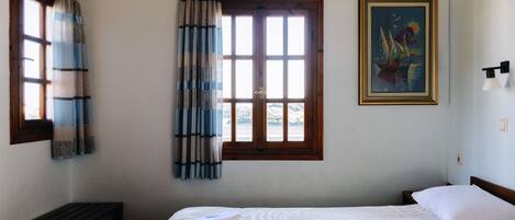 Habitación de hotel con cama, ventana con cortinas, un cuadro en la pared y una mesita de noche.