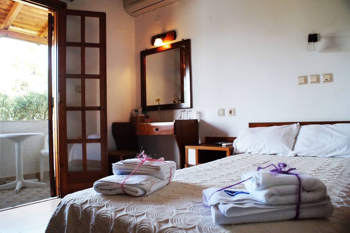 Habitación de hotel con cama, escritorio, silla, espejo y una pequeña mesa.