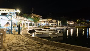 A waterfront restaurant with outdoor seating, boats docked nearby, and a stone-paved walkway. - Drymna Hotel (Dorida)