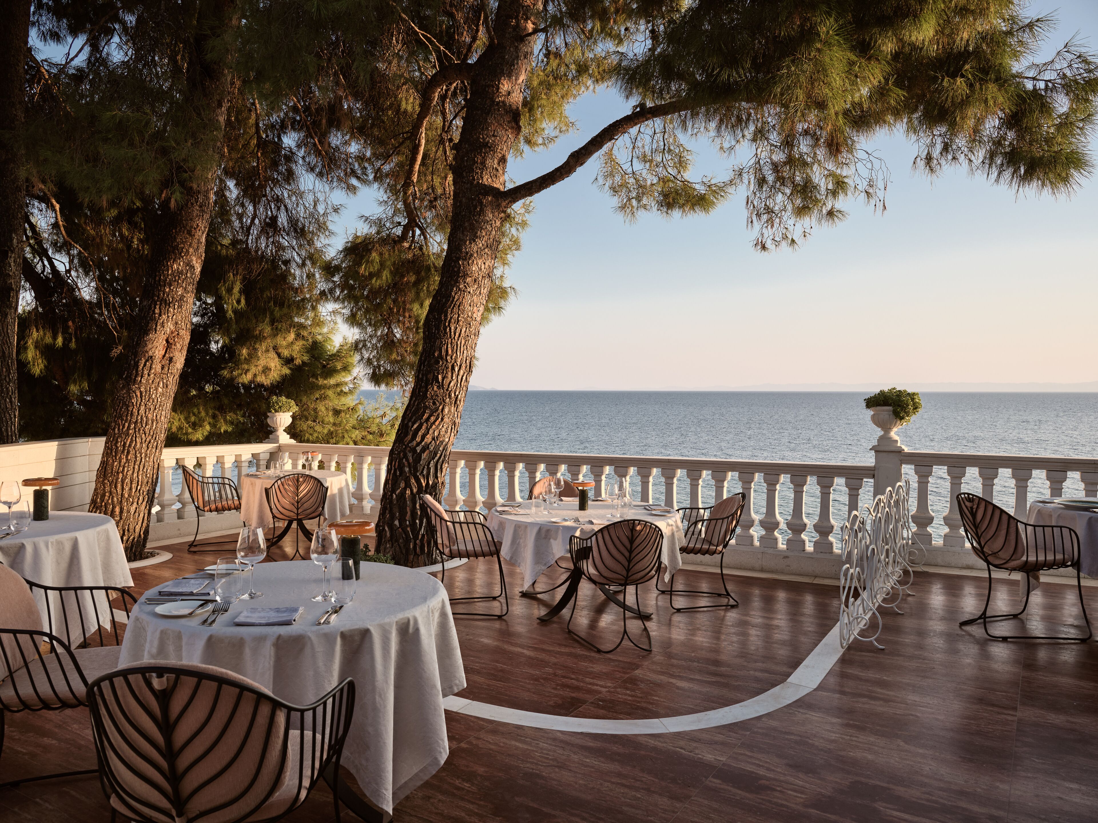 An outdoor dining area with round tables and chairs, overlooking a body of water.