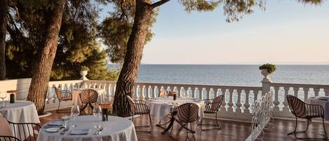 An outdoor dining area with round tables and chairs, overlooking a body of water.