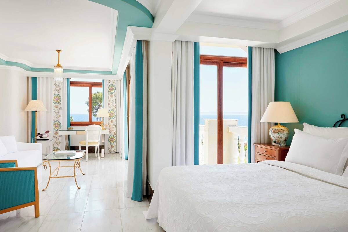 Een hotelkamer met een groot bed, een bureau, een stoel en uitzicht op zee.