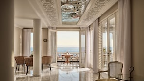 Amplia habitación con vista al mar, con piso de mármol, muebles elegantes y un candelabro.