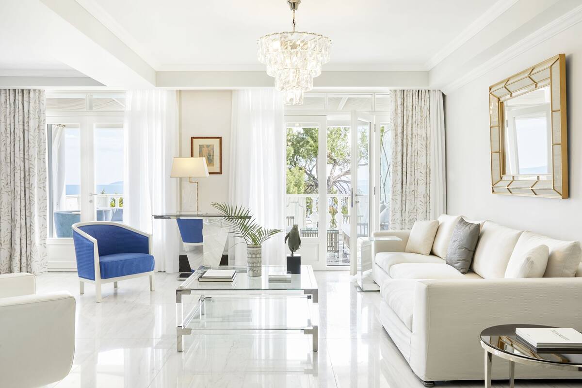 Een moderne woonkamer met een witte bank, een blauwe fauteuil, een glazen salontafel en een kroonluchter.