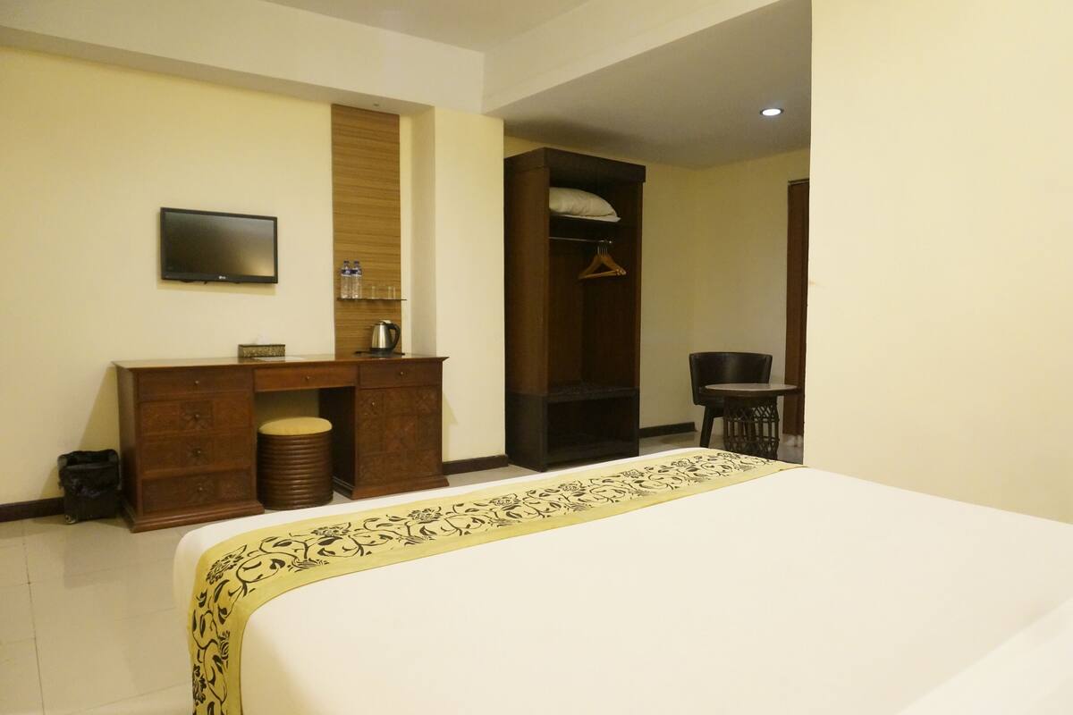 A hotel room with a bed, a desk with a chair, a television, and a wardrobe.