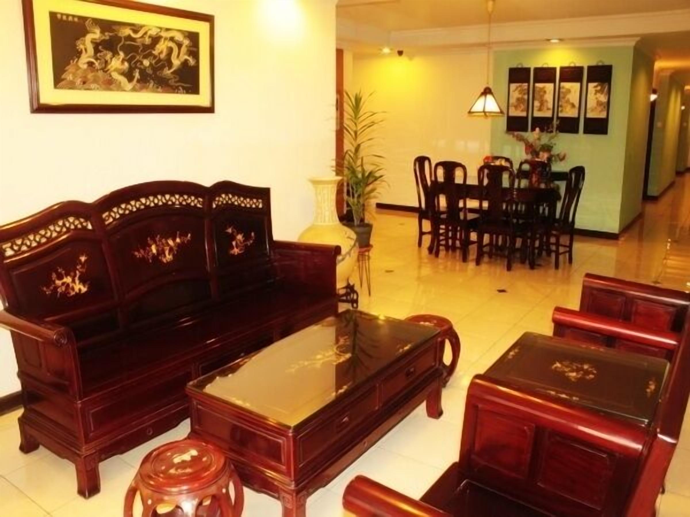 A traditional-style living room with a sofa, coffee table, and chairs. There is a dining area with a table and chairs in the background.