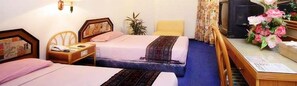 Ein Hotelzimmer mit zwei Betten, einem Schreibtisch mit Computer, einem Stuhl und einer Zimmerpflanze.