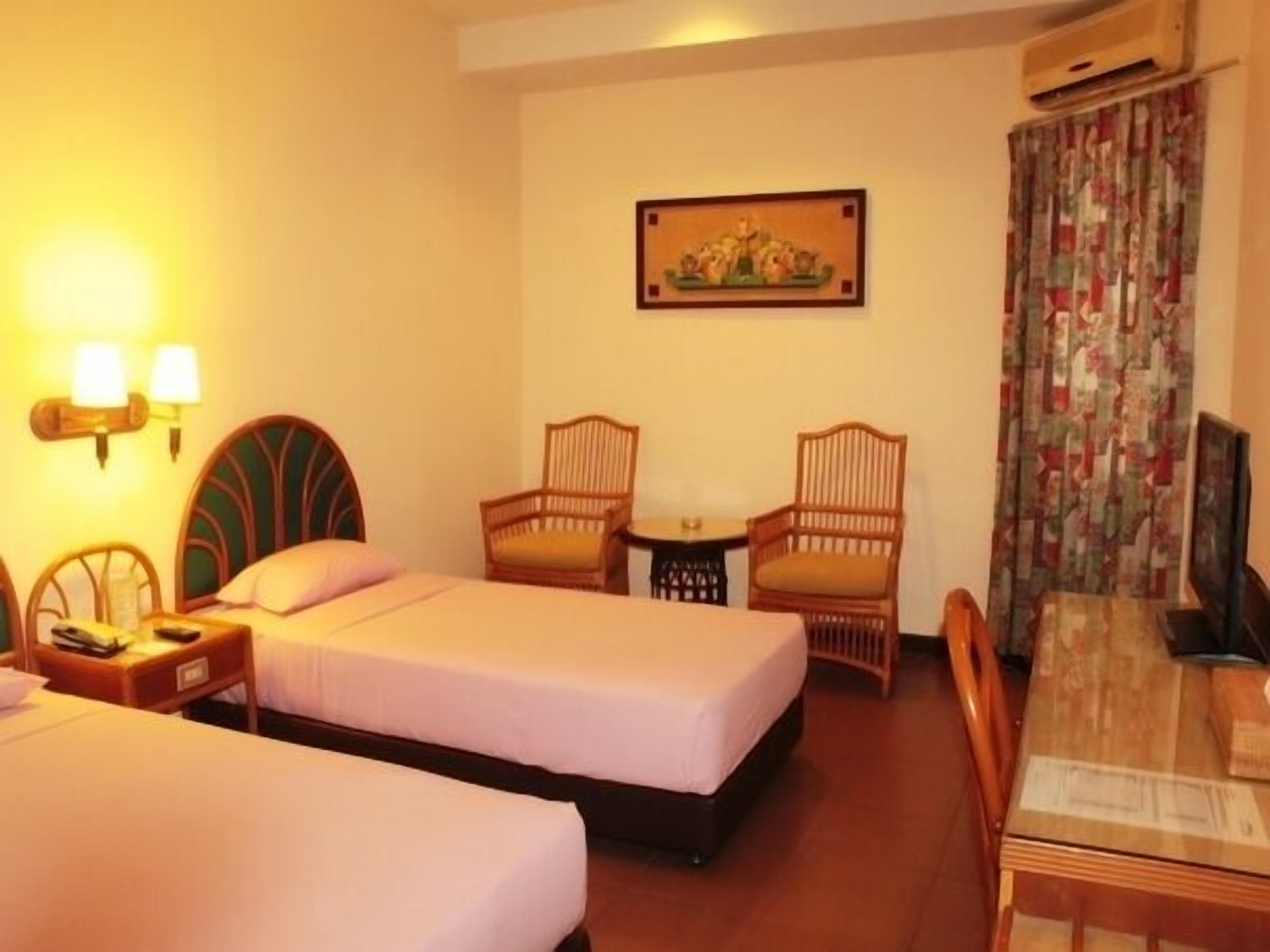 A hotel room with two beds, a small table, two chairs, a painting on the wall, and an air conditioning unit.