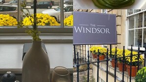A hotel room with a view of a building, a vase with flowers, and a sign reading "The Windsor". - The Windsor Townhouse (Bath)