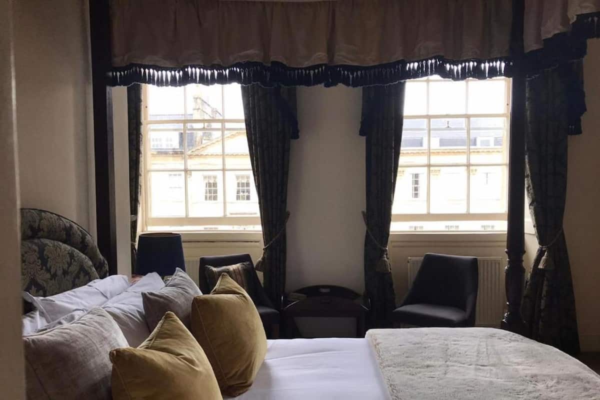 Habitación de hotel con una cama, dos sillones, una mesita y vistas a edificios a través del ventanal.