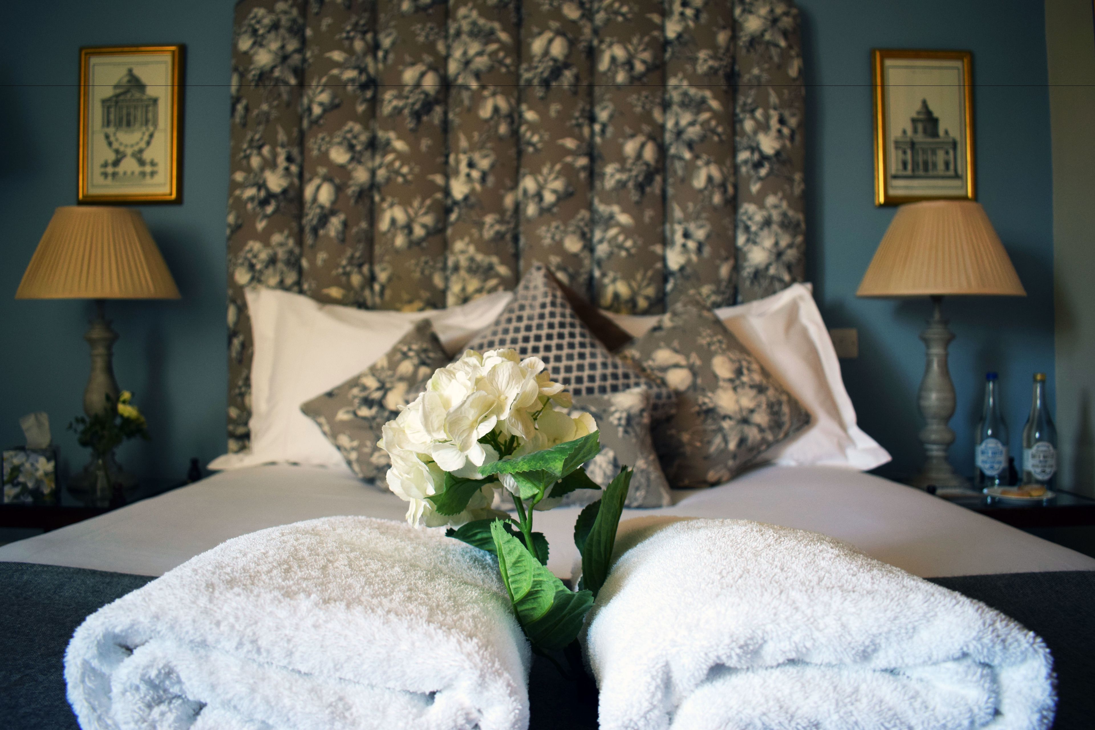 A neatly made bed with white linens, a floral headboard, and two bedside lamps.
